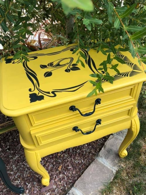 Table de nuit jaune vif avec œuvre d'art noire, entourée de plantes vertes au Petit Nid d'Aigle à Giverny