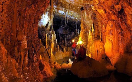 Stunning cave interior with golden stalactites and stalagmites, illuminated pathway for Castellammare del Golfo exploration
