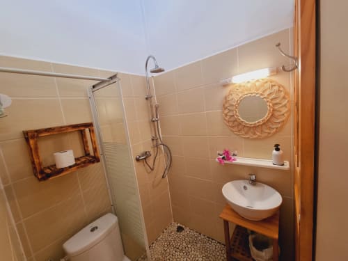 Modern bathroom at Gites Kaladja with shower, vessel sink, beige tiles, and decorative woven mirror