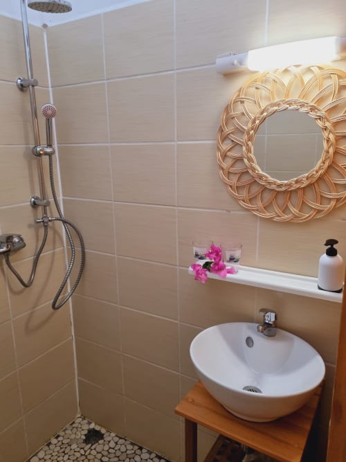Modern bathroom at Gites Kaladja in Port-Louis with round white sink, rainfall shower, decorative mirror, and heated towel