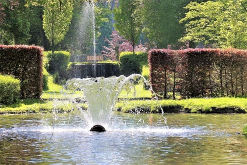 Fontaine dans le bassin de l'hôtel Le Moulin Des Ramiers à Crupet, Belgique, entourée de haies et d'arbres taillés