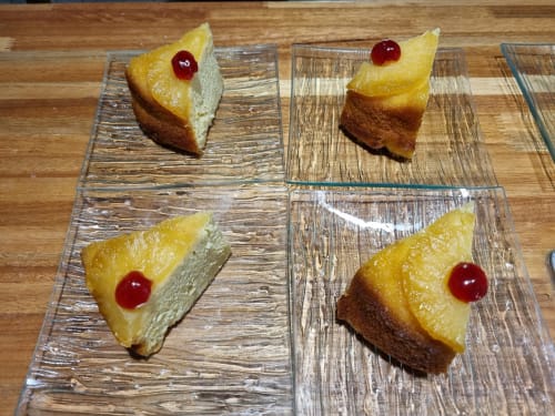 Four slices of pineapple upside-down cake with maraschino cherries on wooden plates at Gites Kaladja in Port-Louis,