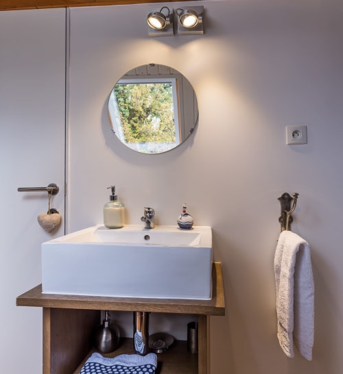 Salle de bain moderne du gîte Vue Sur Gindou avec miroir rond, lavabo sur pied et fenêtre avec vue sur le jardin à Gindou, France