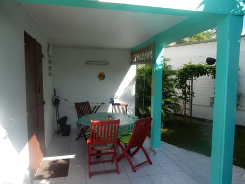 Patio turquoise lumineux avec chaises rouges et table ronde, vue sur le jardin du gîte Caribgites, Sainte-Anne Guadeloupe