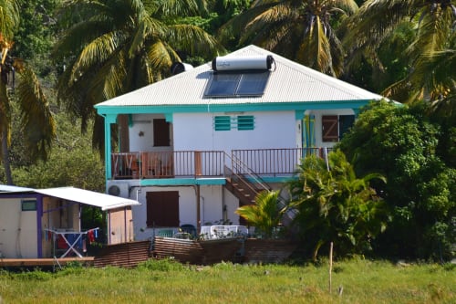 Bungalow bord de mer Caribgites à Sainte-Anne, Guadeloupe avec encadrement turquoise, panneaux solaires et palmiers