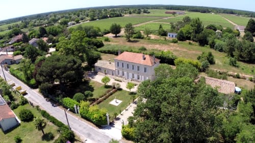 Luftaufnahme des Manoir Lacustre, eines Steinherrenhauses mit Terrakottadach umgeben von Gärten und ländlicher Landschaft in Queyrac