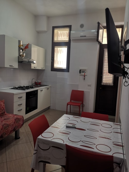 Modern kitchen and dining area with red chairs, white cabinets, and city views at Casa Vacanze Del Golfo apartment in