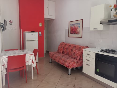Red and white modern kitchen-living area in Castellammare del Golfo apartment with sofa, dining table, and appliances