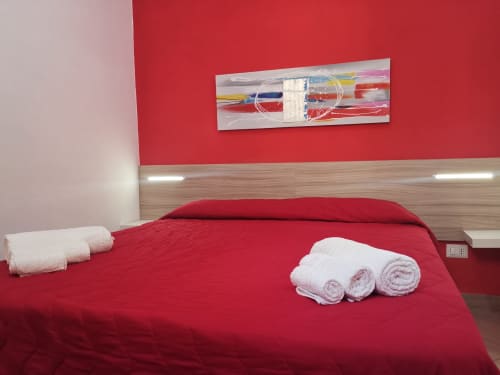 Modern red bedroom with rolled white towels and abstract wall art at Casa Vacanze Del Golfo, Castellammare del Golfo