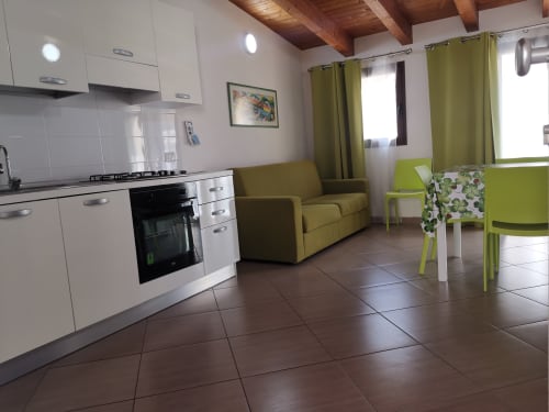 Modern kitchen-living area at Casa Vacanze Del Golfo with white cabinetry, olive green sofa and dining chairs