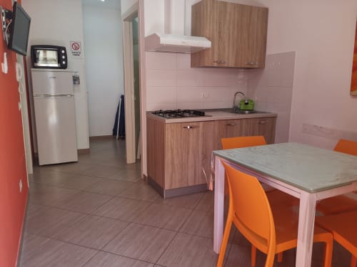 Modern kitchen with wooden cabinets, pink tiles, dining table with orange chairs at Casa Vacanze Del Golfo, Castellammare del