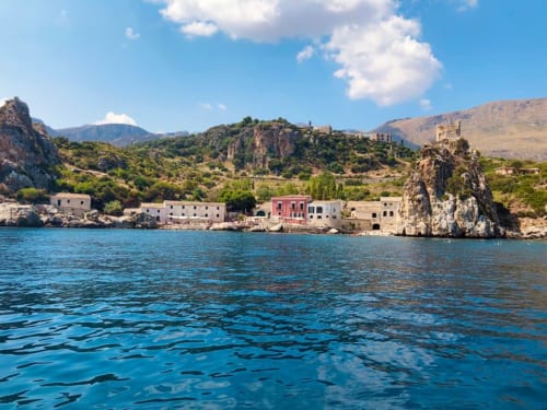 Coastal view of Castellammare del Golfo with colorful buildings, rocky cliffs, and azure Mediterranean waters