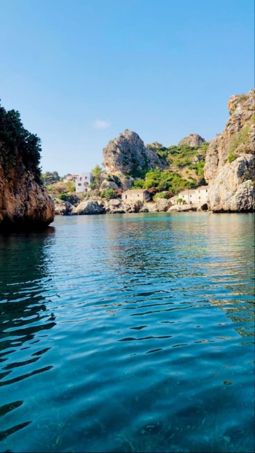 Turquoise waters of Castellammare del Golfo with rocky cliffs and traditional stone houses nestled in the Italian coastline