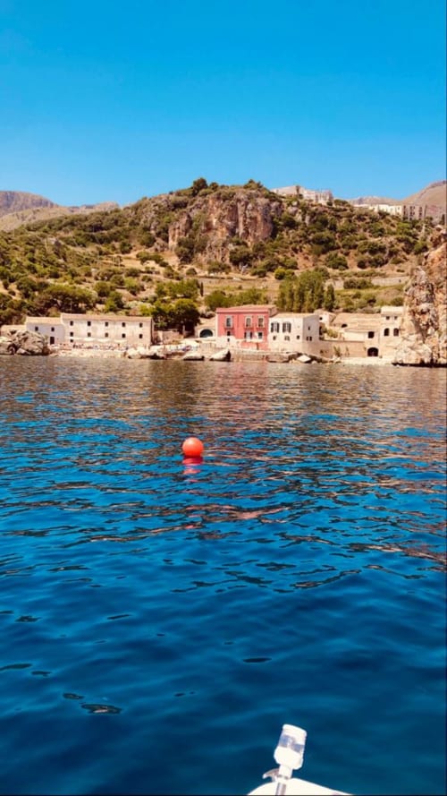 Red buoy floating in blue Mediterranean waters near colorful waterfront buildings in Castellammare del Golfo