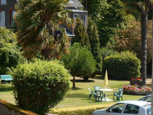 Jardin luxuriant à L'Abri Des Vents avec palmiers, haies taillées, coin détente et bâtisse historique