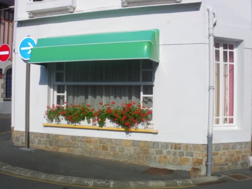 Devanture de L'Abri Des Vents à Saint-Jean-le-Thomas avec auvent vert et jardinières de fleurs rouges