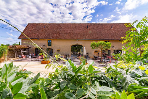 Charming B&B courtyard in Gindou, France with rustic stone building, terrace seating, and lush gardens
