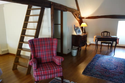 Rustic loft bedroom at Le Fassardy B&B in Châteauroux with red plaid armchair, wooden beams, and ladder staircase