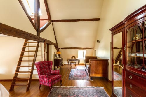 Spacious loft bedroom at Le Fassardy B&B in Châteauroux with exposed beams, red plaid armchair, and wooden furnishings