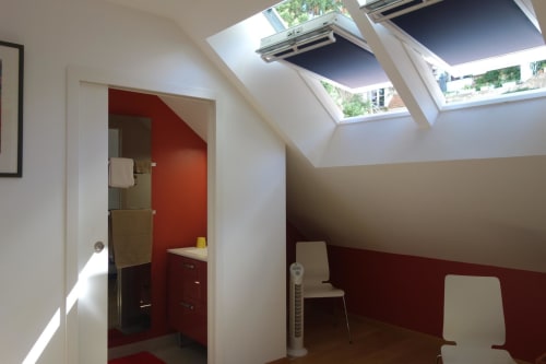 Intérieur de cottage moderne avec puits de lumière, mur d'accent rouge, poutres blanches et vue sur le jardin au Fassardy à Châteauroux