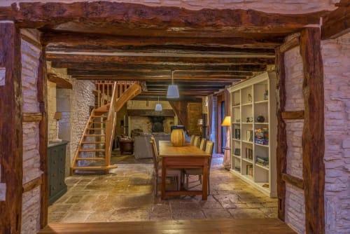 Intérieur rustique du gîte Vue Sur Gindou avec poutres apparentes, table de salle à manger en bois, murs de pierre et bibliothèque à Gindou,