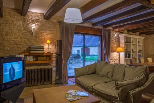 Salon cosy de Vue Sur Gindou avec briques apparentes, cheminée, canapé vert et vue sur le jardin par grandes fenêtres