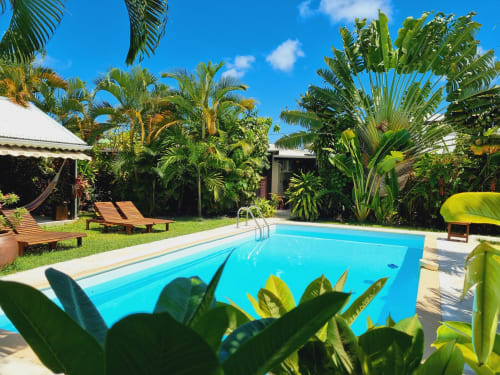 Tropical swimming pool at Gites Kaladja BnB in Port-Louis, surrounded by palm trees and wooden lounge chairs