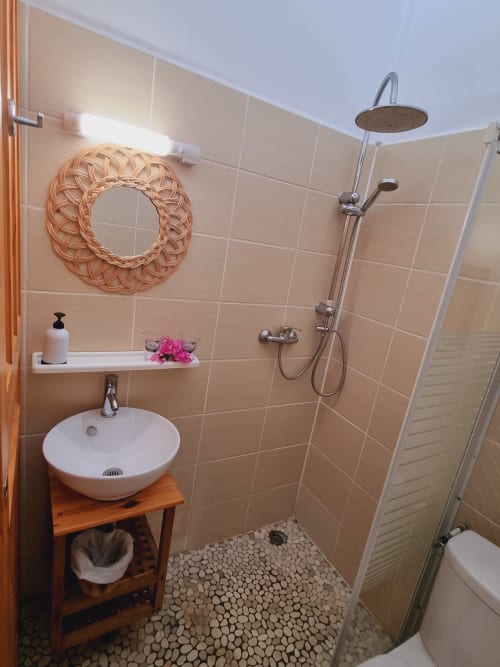 Modern bathroom at Gites Kaladja with round vessel sink, walk-in shower, decorative wreath, and pebble tile floor