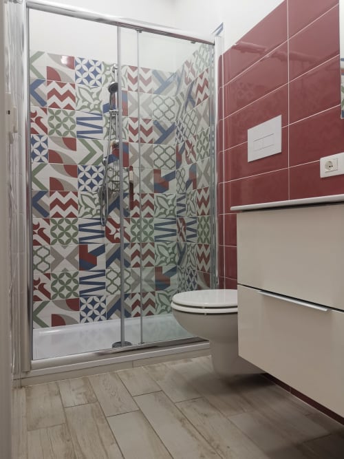 Modern bathroom with colorful geometric tile shower, red walls, white toilet, and wood-look flooring at Casa Vacanze Del