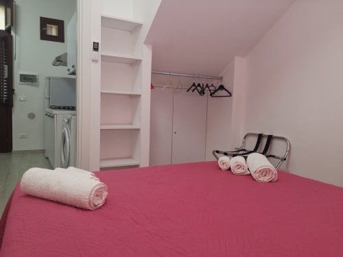 Pink bedroom in Castellammare del Golfo apartment with bed, rolled towels, shelving, washer, and hangers