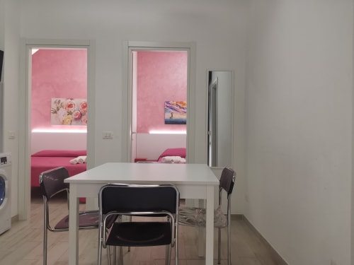 Modern apartment dining area with white table and black chairs opening to pink-themed bedroom at Casa Vacanze Del Golfo in