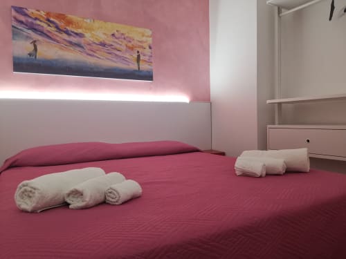Modern bedroom with pink walls, red bedding, rolled towels, and sunset artwork at Casa Vacanze Del Golfo apartment in