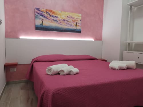 Modern bedroom in Apartment Rose at Casa Vacanze Del Golfo with pink walls, white headboard, rolled towels on magenta