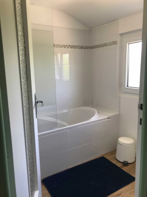 Salle de bain moderne avec douche vitrée, baignoire blanche et accents de carrelage au gîte Les Gîtes De L'odet