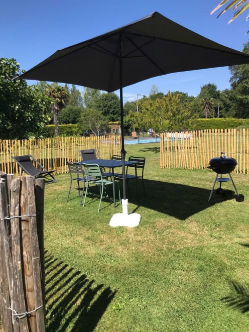 Espace de détente extérieur aux Gîtes De L'odet avec parasol noir, table à manger, transats et barbecue