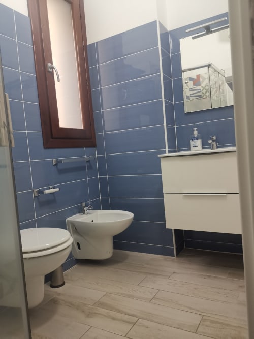 Modern bathroom with blue tile walls, white toilet and bidet, vanity sink, and mirror in Apartment Sea at Casa Vacanze Del