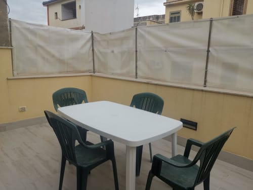 Rooftop terrace dining area with white table, dark green chairs, and translucent privacy screens at Casa Vacanze Del Golfo