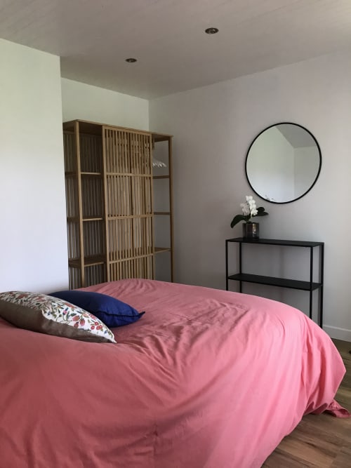 Chambre moderne avec literie rose, paravent en bois, miroir rond et console noire aux Gîtes De L'odet