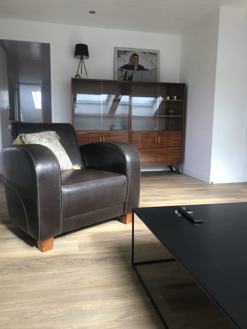 Salon moderne avec fauteuil en cuir noir, meuble en bois et télévision écran plat aux Gîtes De L'odet