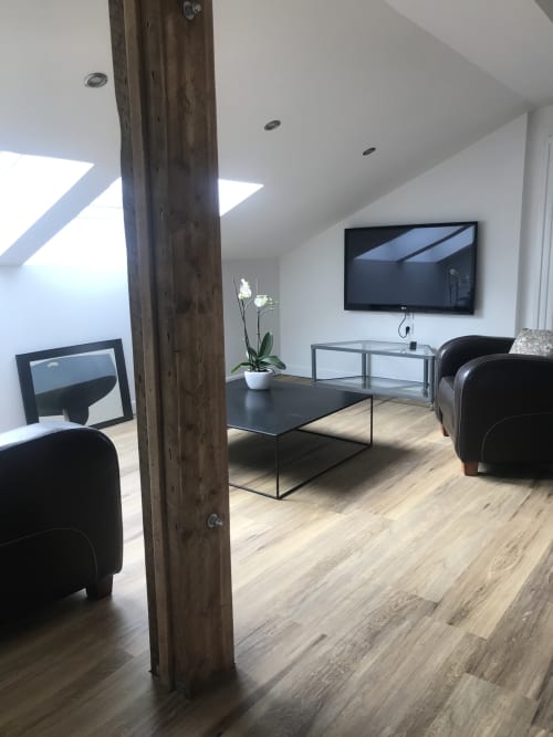 Espace séjour de loft moderne avec fauteuils noirs, télévision écran plat et poutre en bois aux Gîtes De L'odet,