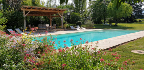 Piscine turquoise du Château de Grandmont B&B à Blacé, France, avec pergola en bois, chaises longues et jardins fleuris