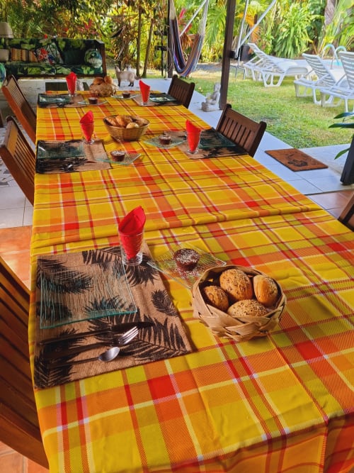 Outdoor dining setup at Gites Kaladja in Port-Louis with bright yellow plaid tablecloth, place settings, and tropical garden