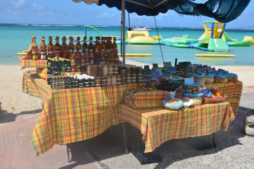 Étal de vendeur sur la plage à Sainte-Anne avec nappes colorées présentant l'artisanat local et boissons près des eaux turquoise des Caraïbes