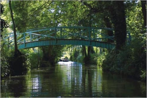 Pont turquoise en arche enjambant un canal tranquille à travers les arbres verdoyants des Marais Poitevin