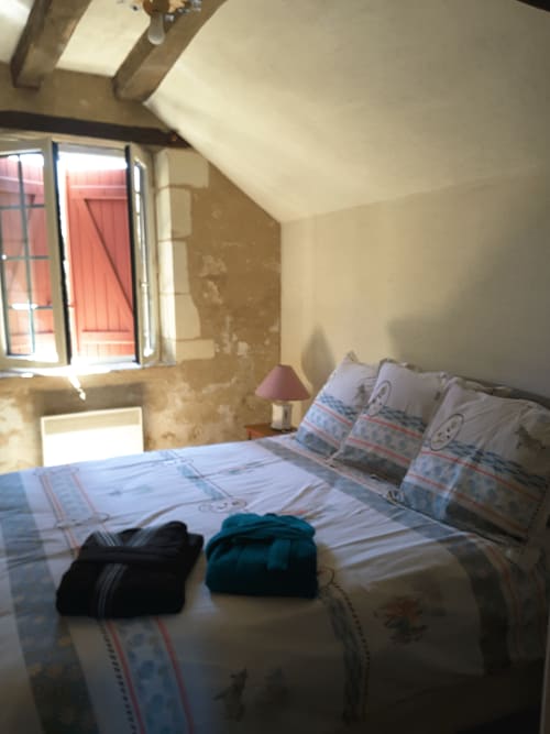 Attic bedroom at Château de Ré with sloped ceilings, beamed ceiling, striped bedding, and window overlooking courtyard in Le
