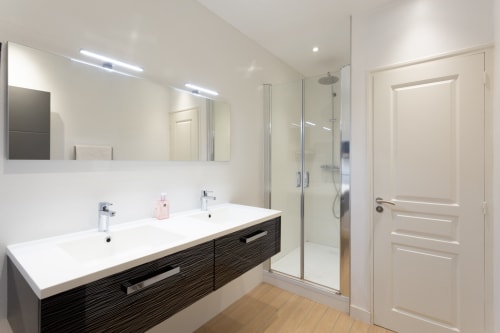 Modern bathroom in Manoir de la Nogrie with dual sink vanity, glass shower enclosure, and rainfall showerhead in Val d'Izé