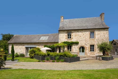 Manoir de la Nogrie stone manor house with manicured gardens in Val d'Izé, France, under clear blue sky