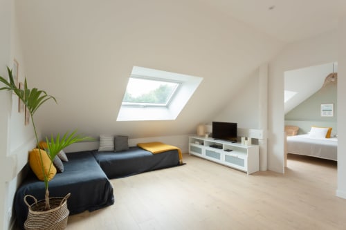 Bright attic bedroom at Manoir de la Nogrie with skylight, dark sofa, TV, and en-suite bedroom visible in Val d'Izé