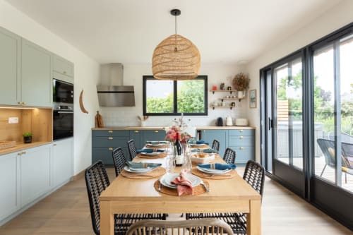 Modern kitchen-dining area at Manoir de la Nogrie with wooden table, blue cabinetry, and panoramic doors overlooking Val