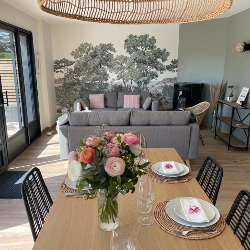 Elegant dining area at Manoir de la Nogerie with fresh pink flowers, wooden table, and forest mural backdrop